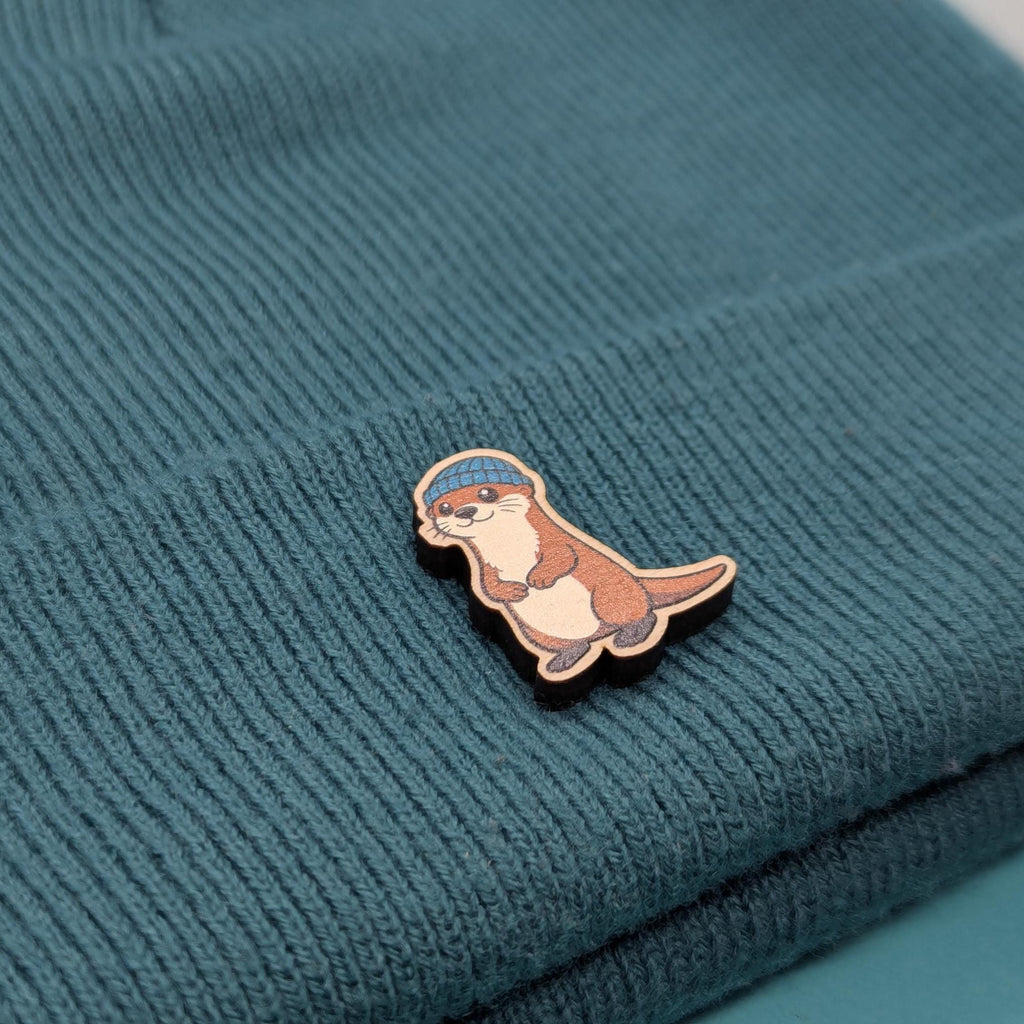 Wooden pin of a cartoon otter on a textured teal fabric background