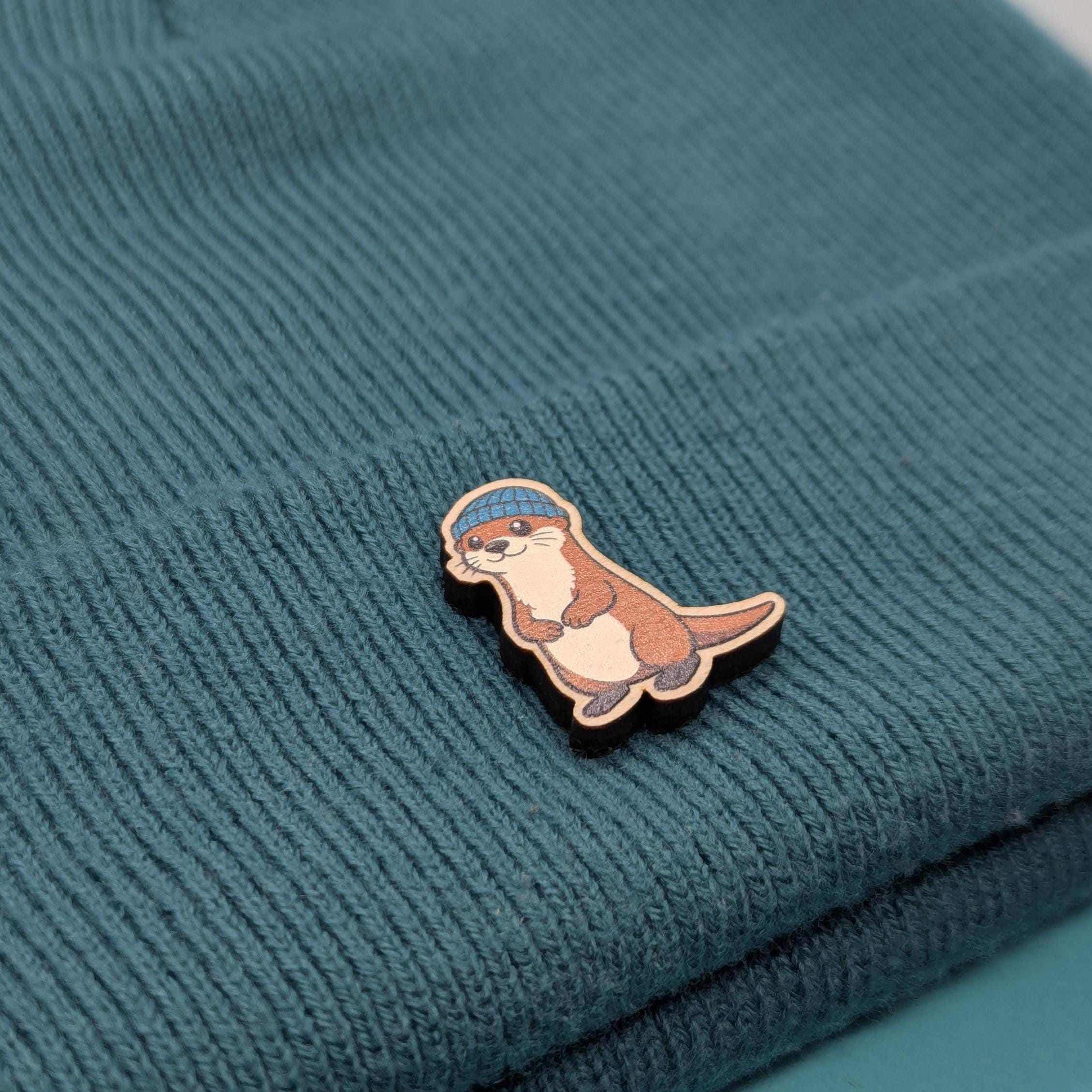 Wooden pin of a cartoon otter on a textured teal fabric background