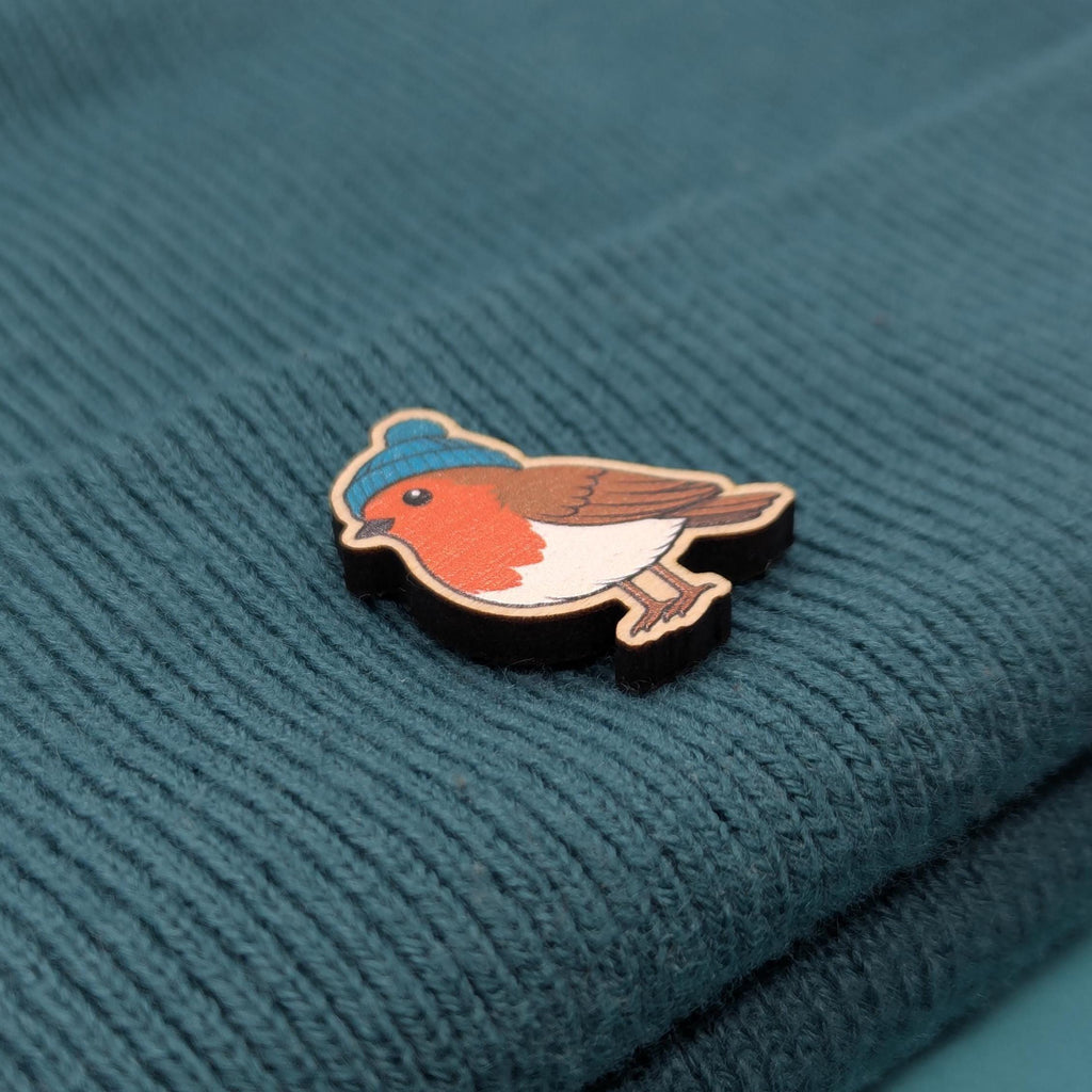 Robin wooden pin badge on a textured teal fabric background