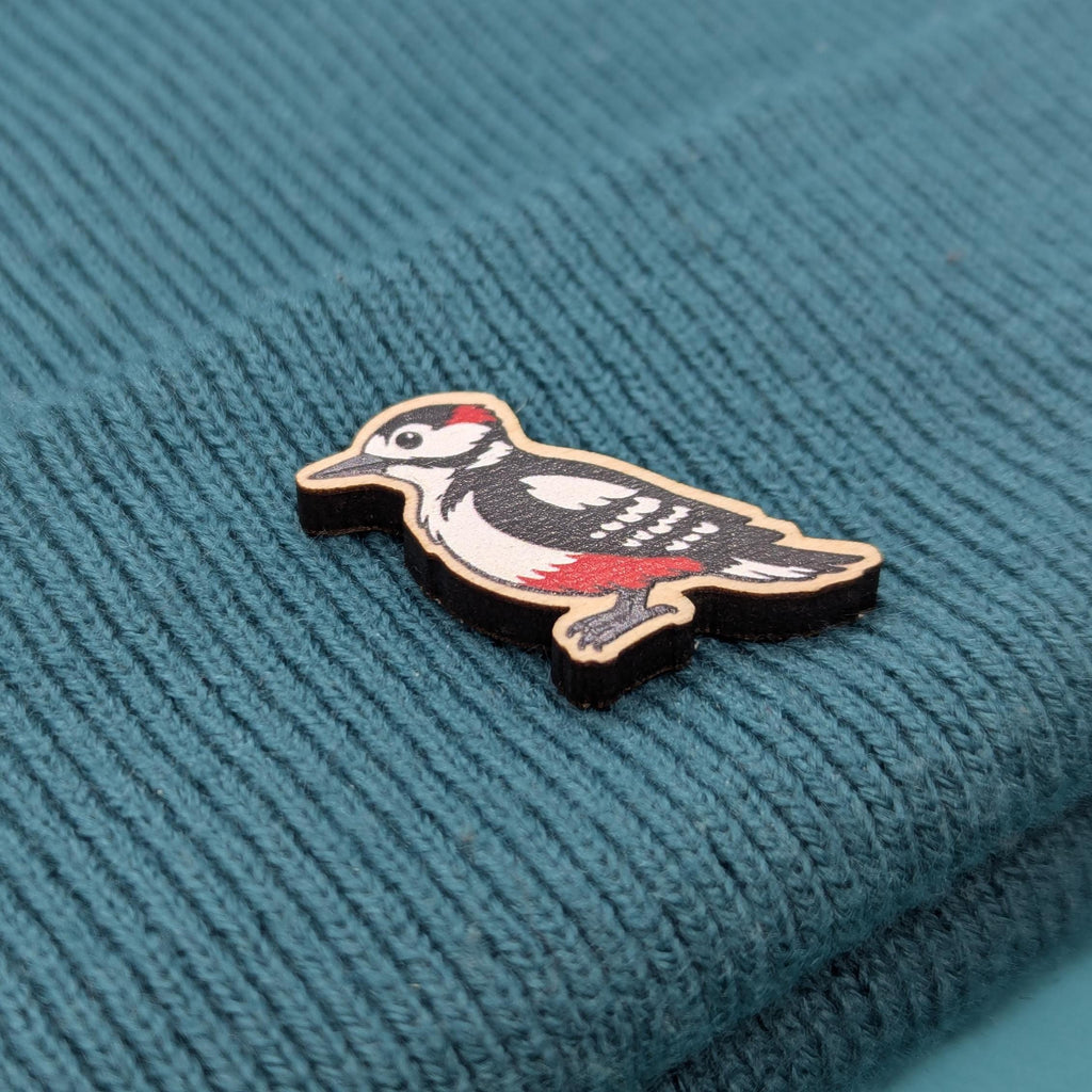Woodpecker-shaped wooden pin on a textured teal fabric background