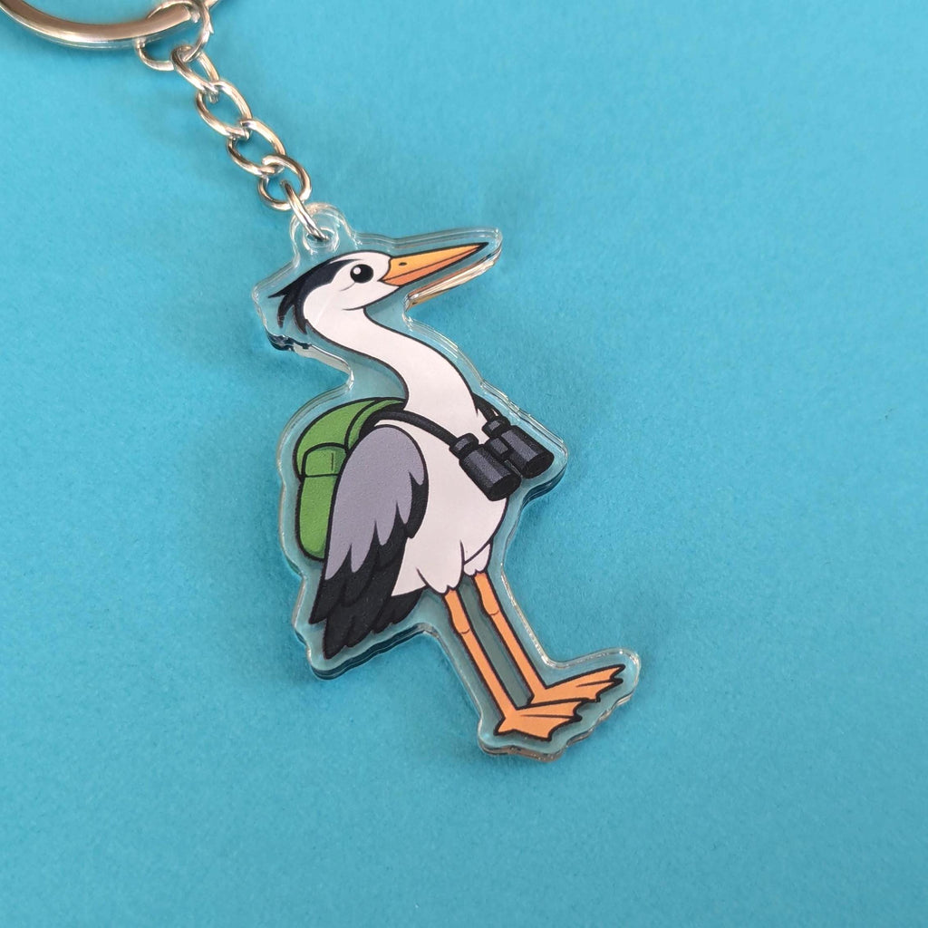 Keychain with a cartoon heron carrying a green bag on a blue background