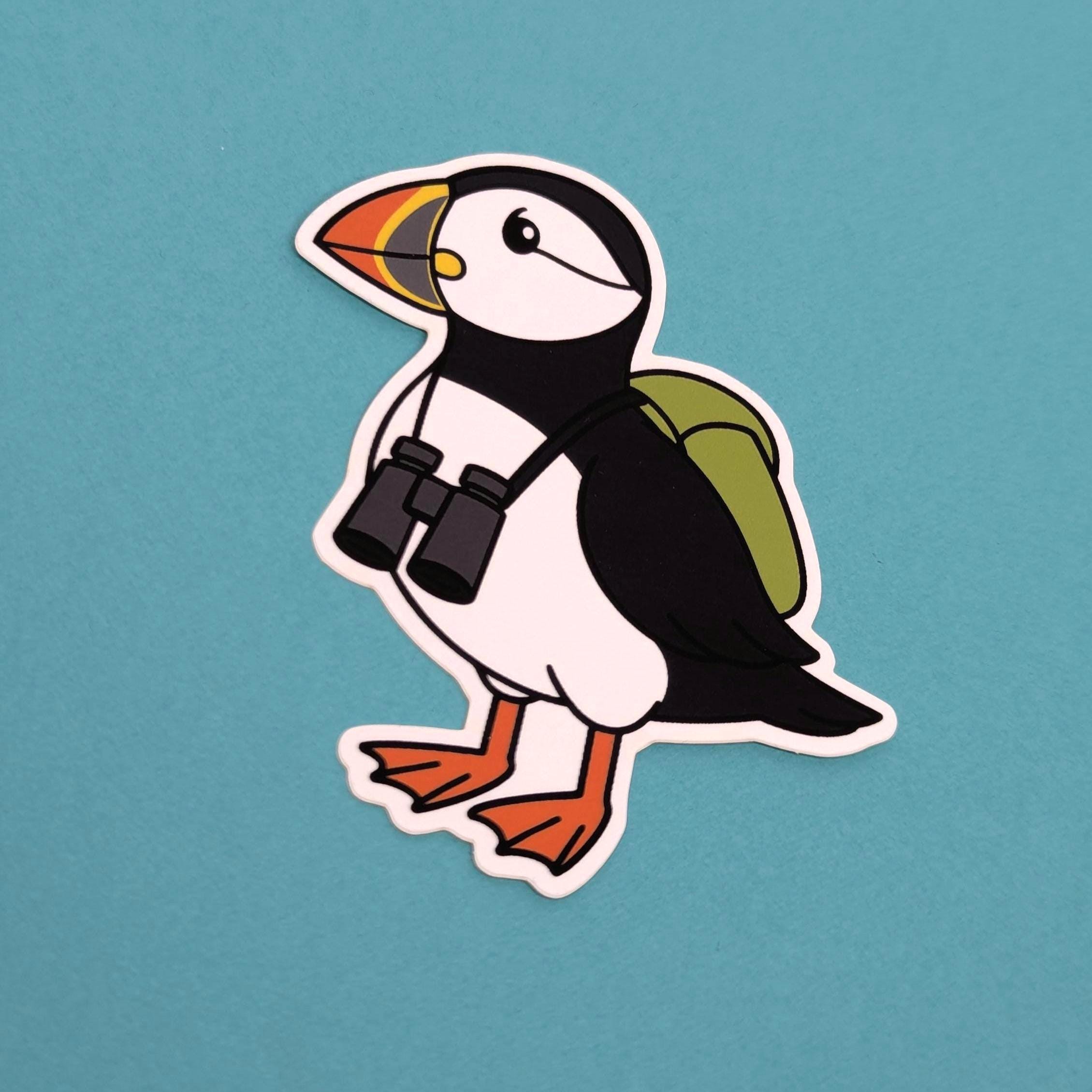 Sticker of a puffin with binoculars and a backpack on a blue background