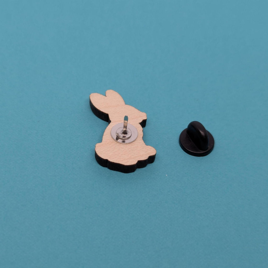 Back of wooden bunny pin with a black clutch back on a blue background