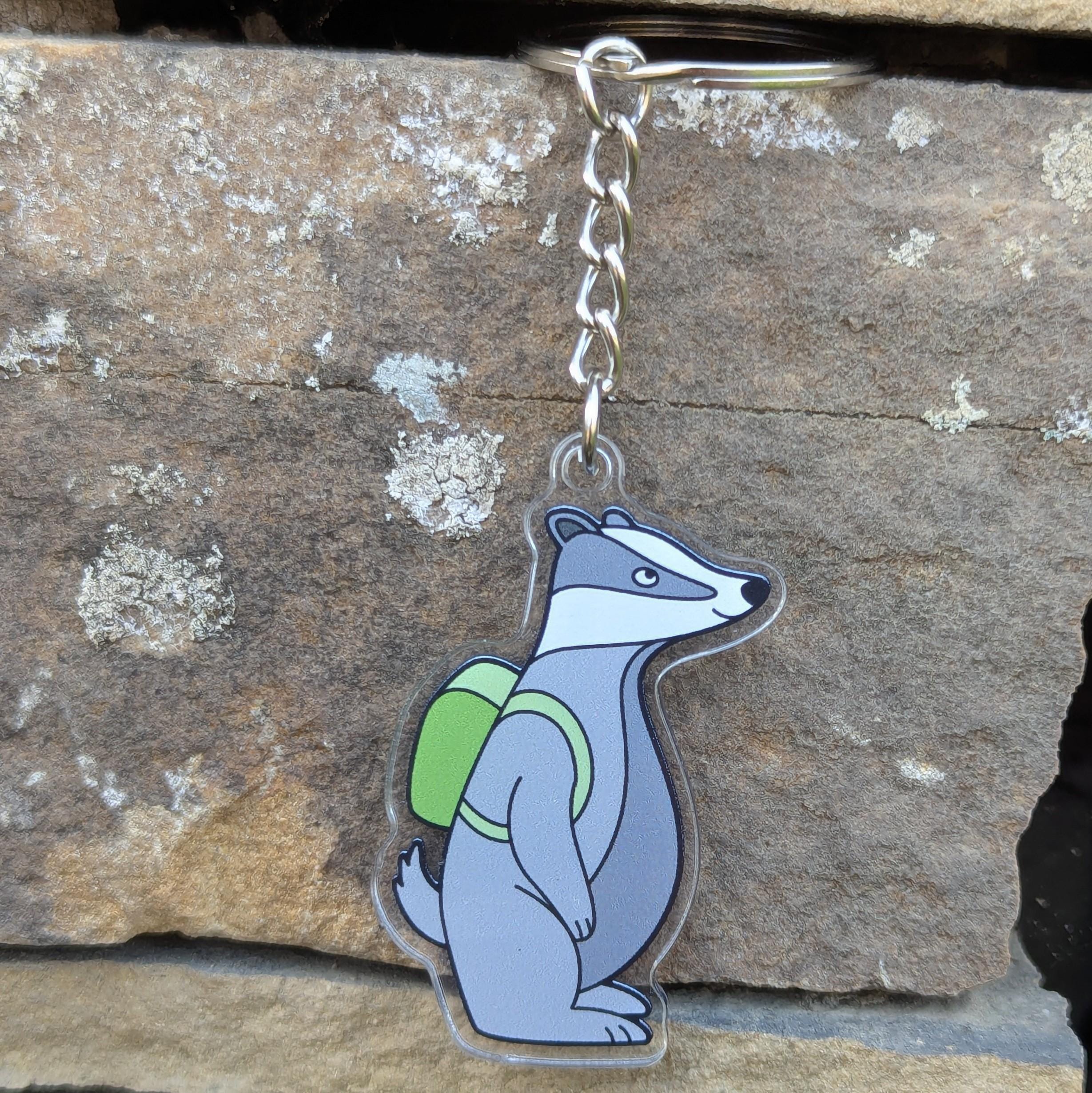 Keychain with a badger wearing a green backpack on a stone surface