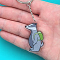 Keychain with a cartoon badger design held in a hand against a teal background