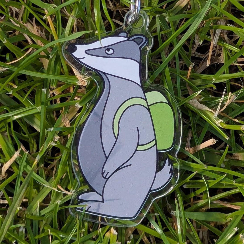 Keychain of a badger with a green backpack on grass