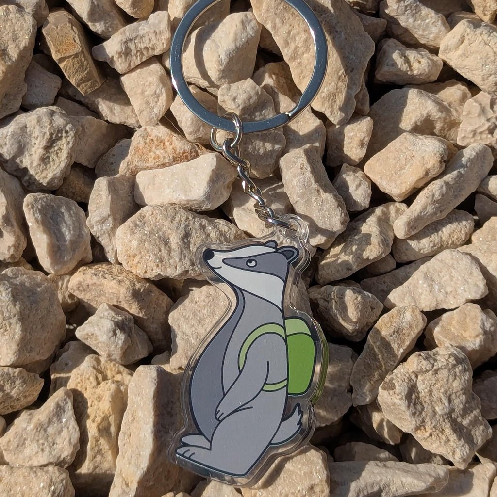 Keychain with a bear design wearing a green backpack on a rocky surface
