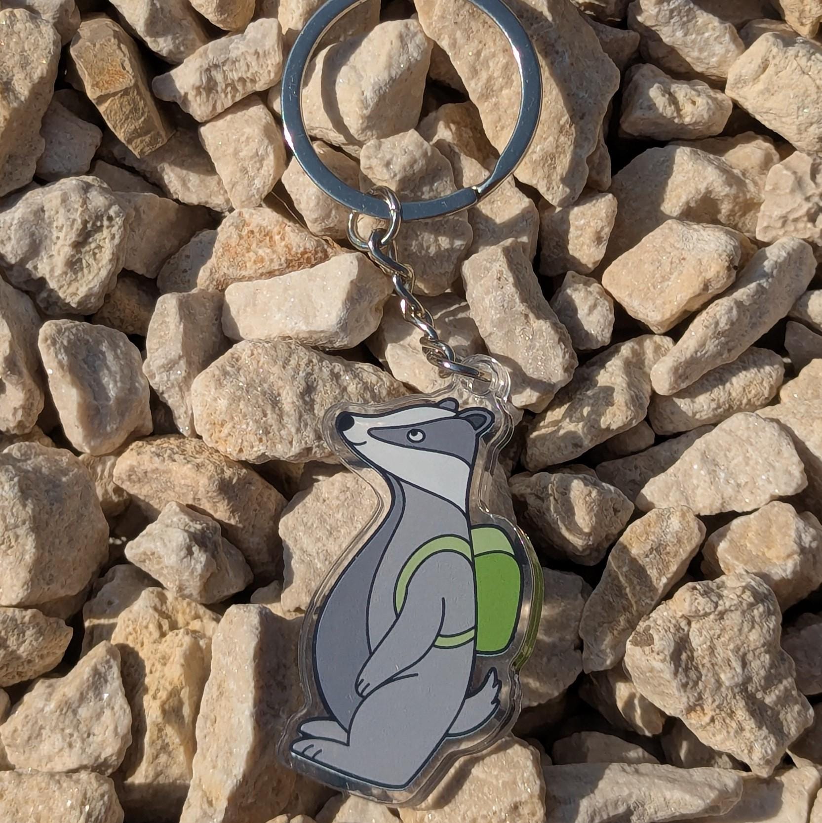 Keychain with a bear design wearing a green backpack on a rocky surface