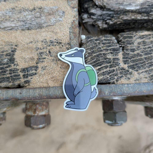 Badger magnet with a green backpack on a metal surface with stones in the background
