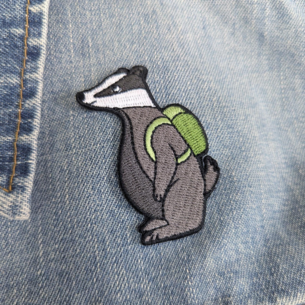 Embroidered badger patch with a green backpack on denim fabric
