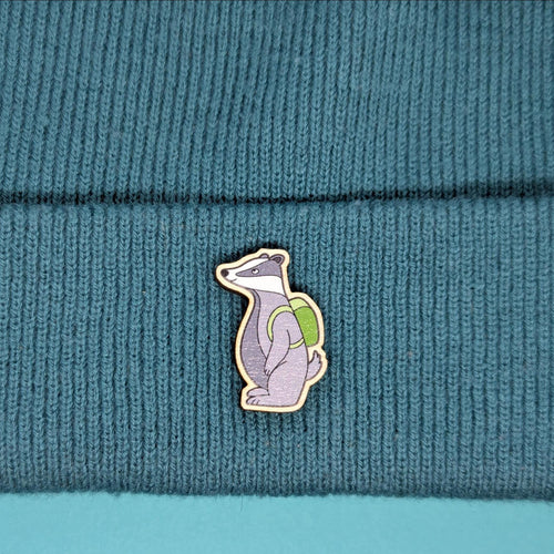 badger wooden pin with a backpack on a teal knitted fabric background