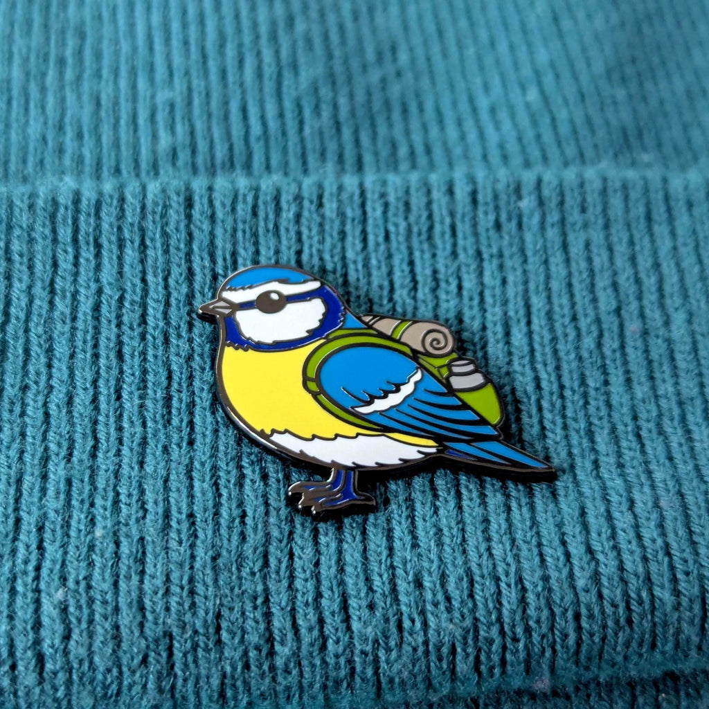 blue tit enamel pin on a textured teal fabric background
