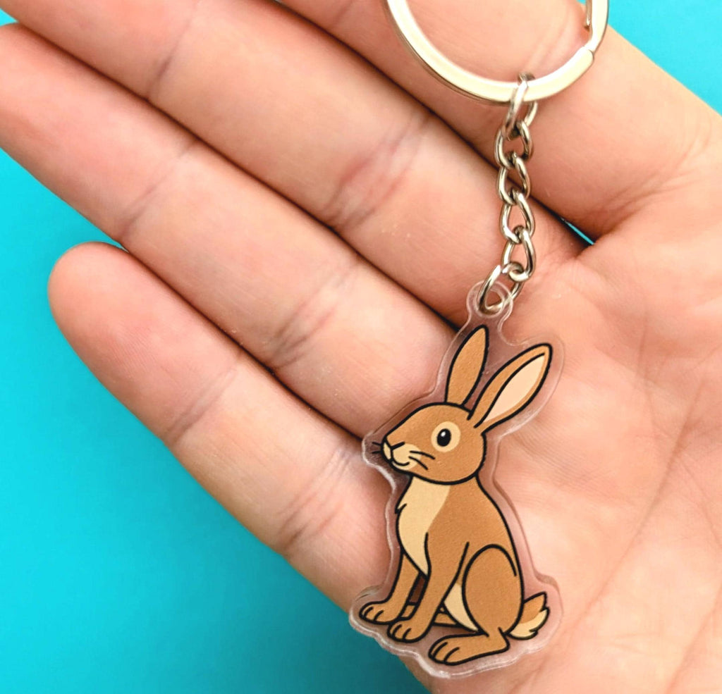 Hand holding a brown hare keychain against a blue background