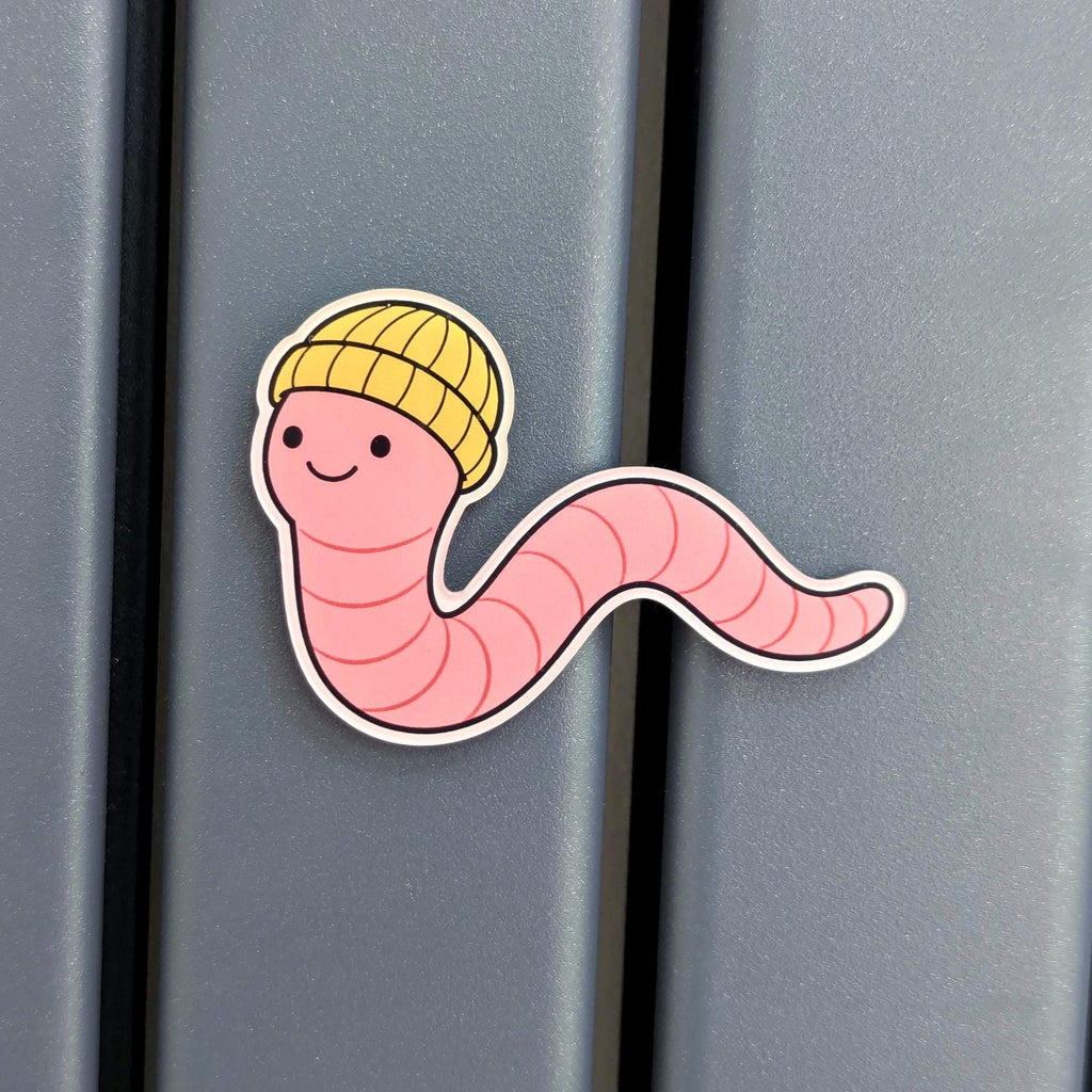 Refrigerator magnet of a cartoon worm wearing a yellow hat on a metallic surface