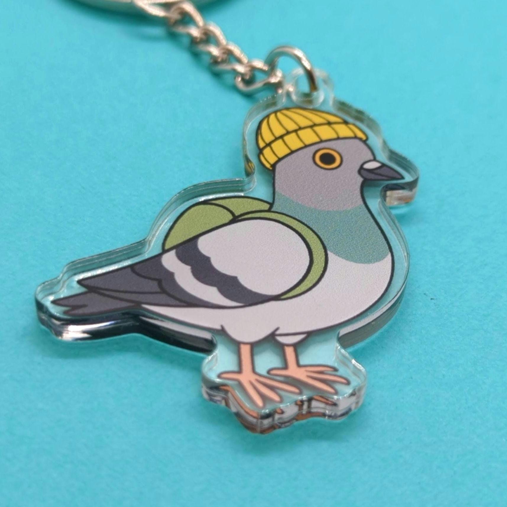 Keychain with a pigeon design wearing a yellow beanie on a blue background