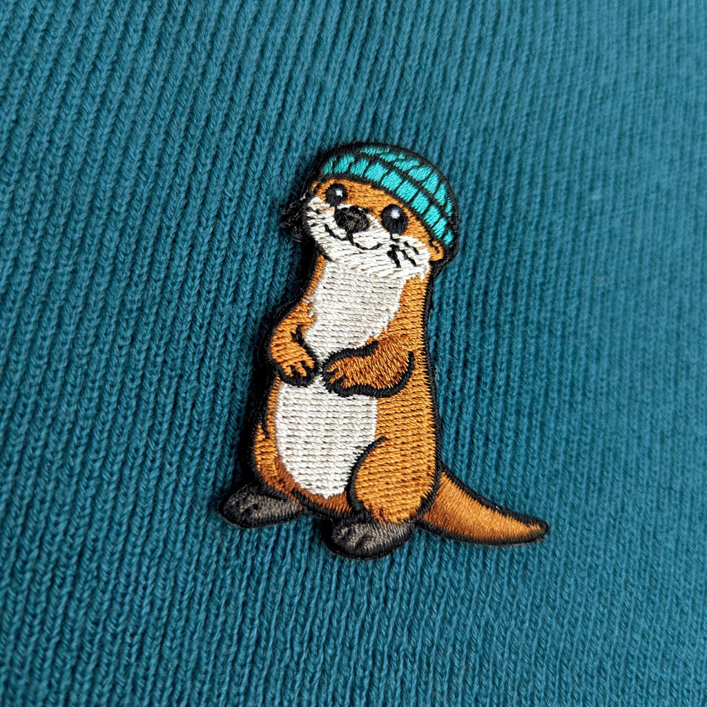 Embroidered otter wearing a blue hat on a teal fabric background