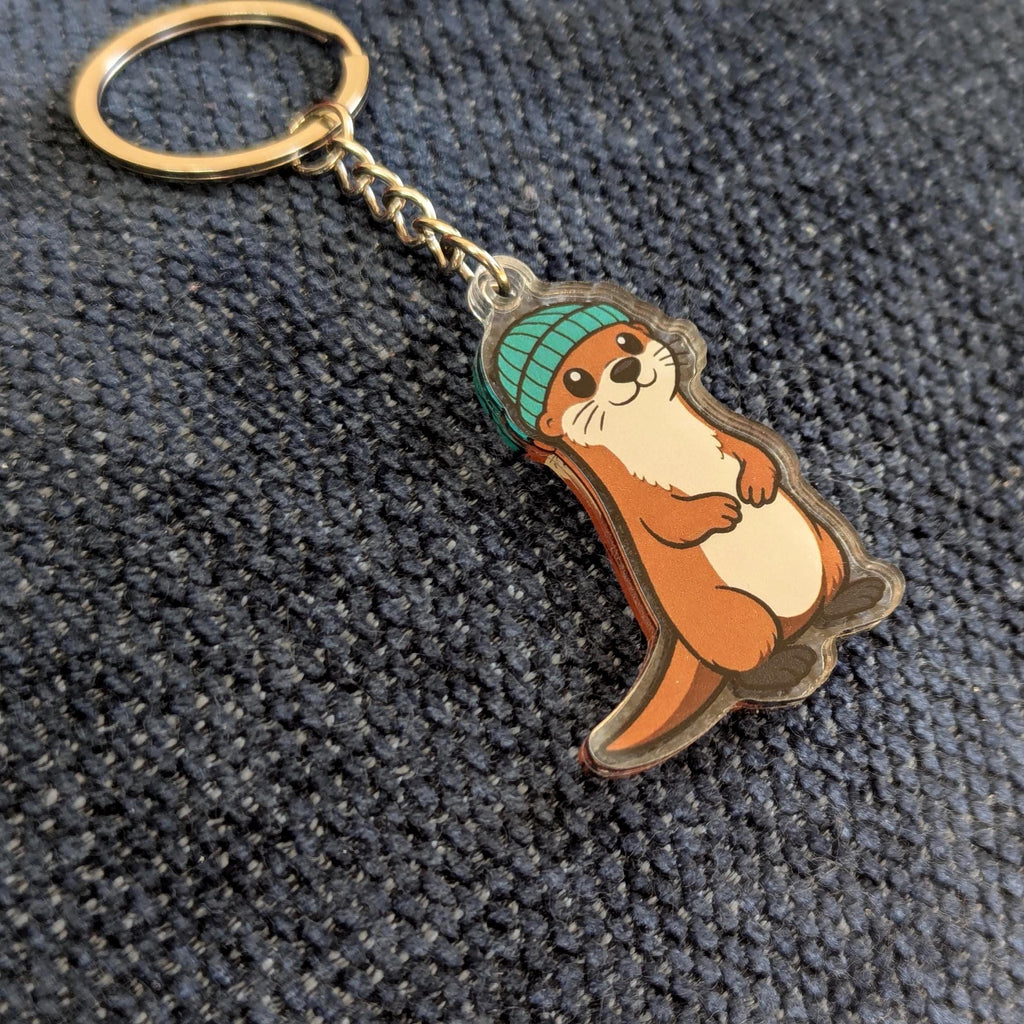 Keychain with a cartoon otter wearing a green beanie on a textured surface