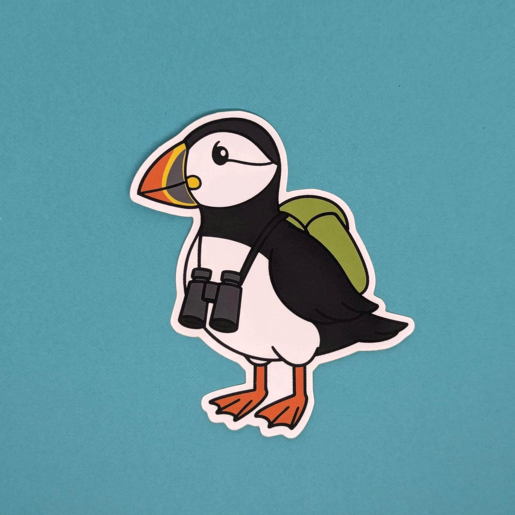 Sticker of a puffin with a backpack and binoculars on a teal background