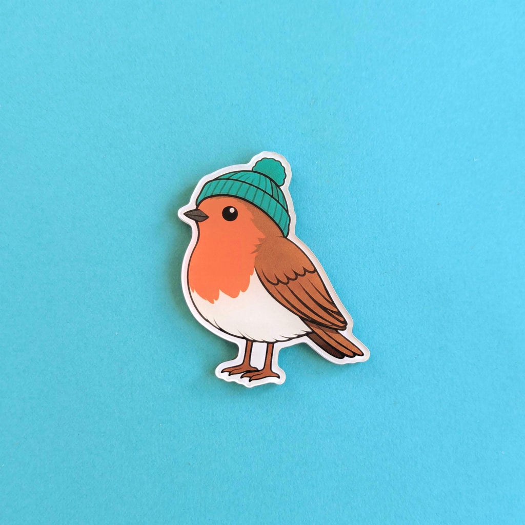 Fridge magnet of a bird wearing a green beanie on a blue background