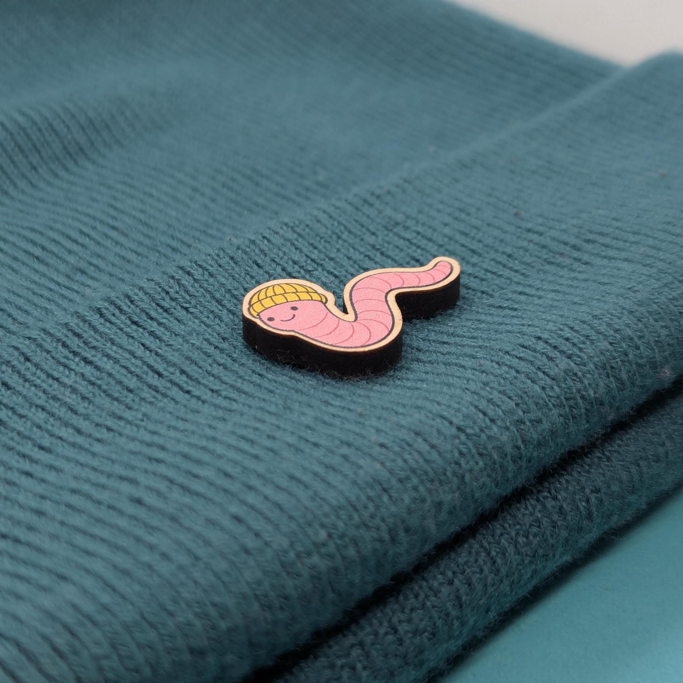 Pink cartoon-style worm wooden pin on a teal fabric background
