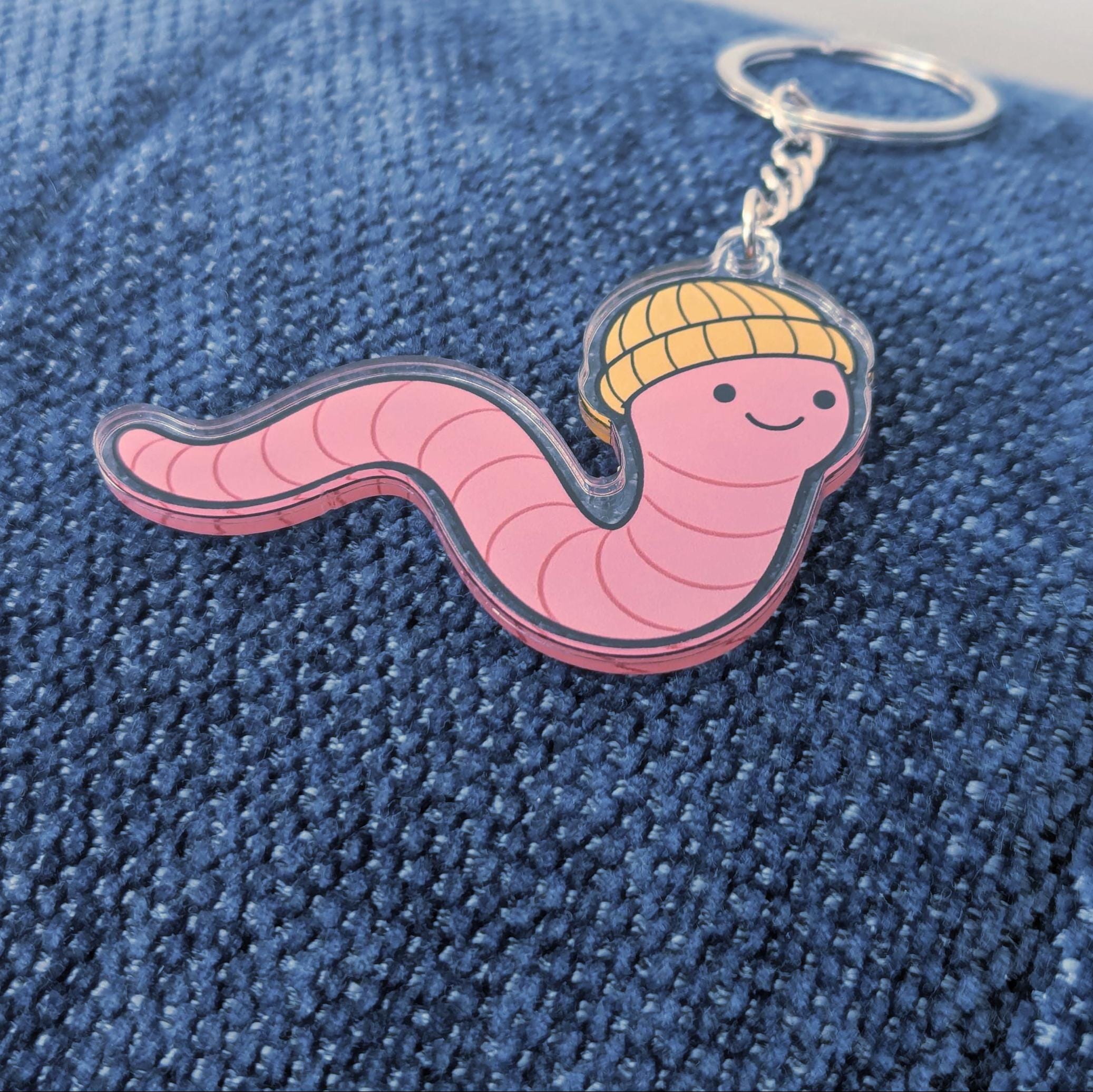 Keychain shaped like a pink worm with a yellow hat on a blue denim background