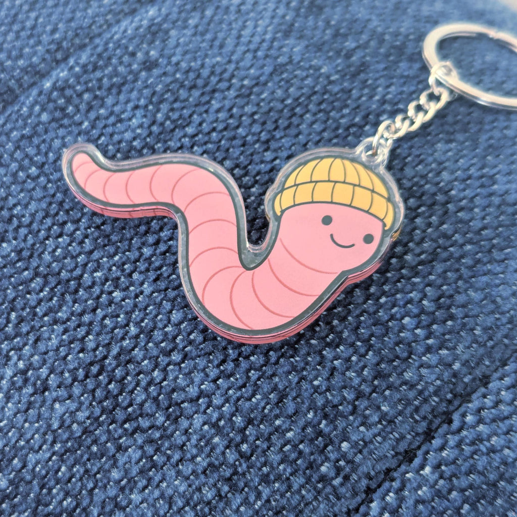 Keychain shaped like a pink worm with a yellow beanie on a blue denim background
