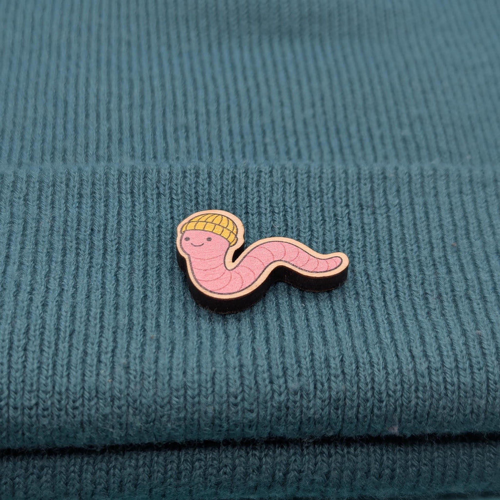 Wooden pin with a cartoonish worm design on a textured teal fabric background