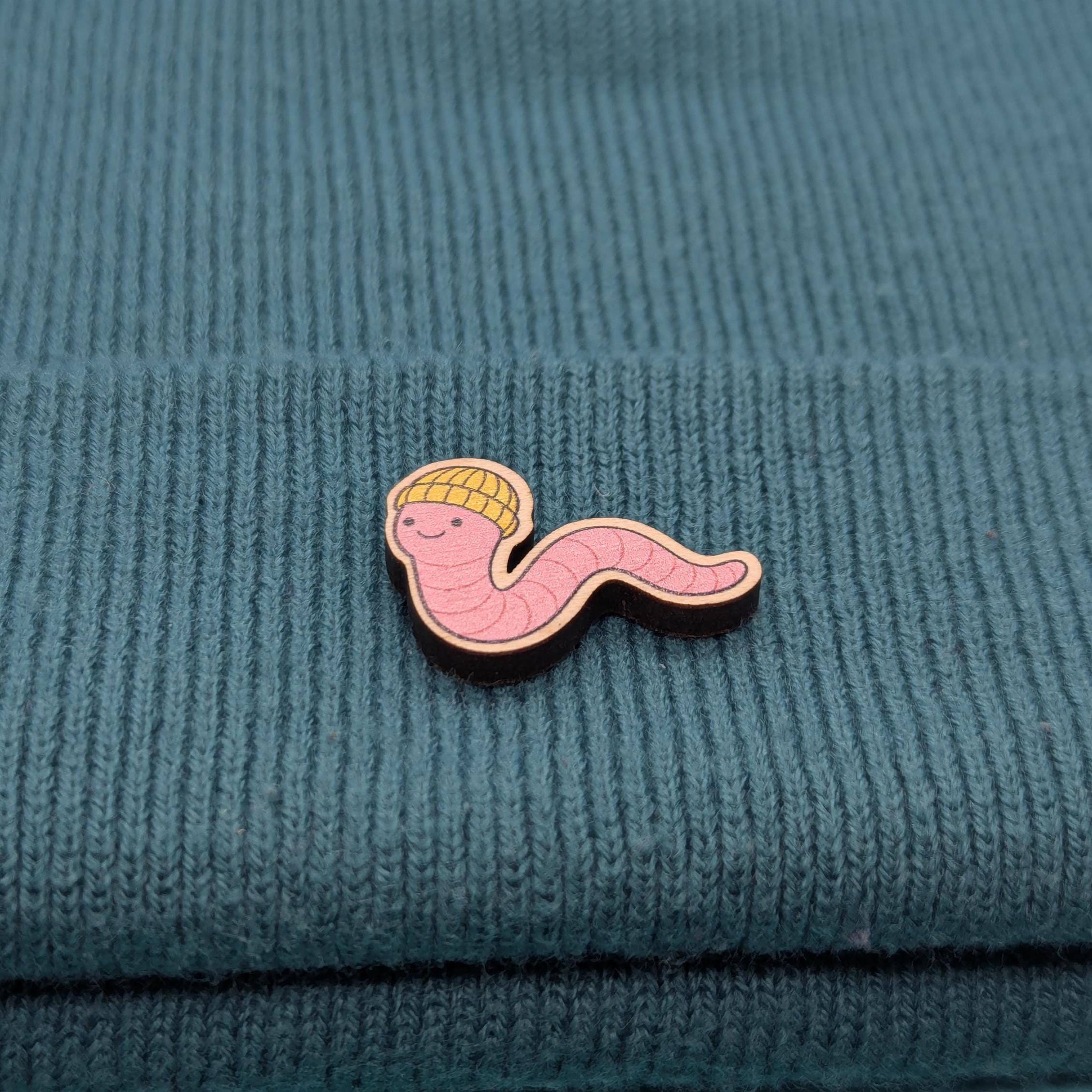 Wooden pin with a cartoonish worm design on a textured teal fabric background