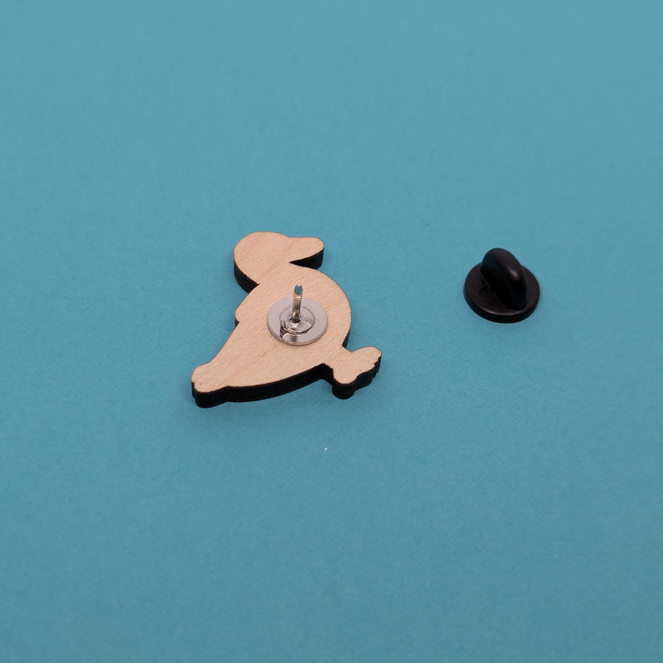 Wooden duck pin back with a black clutch on a blue background