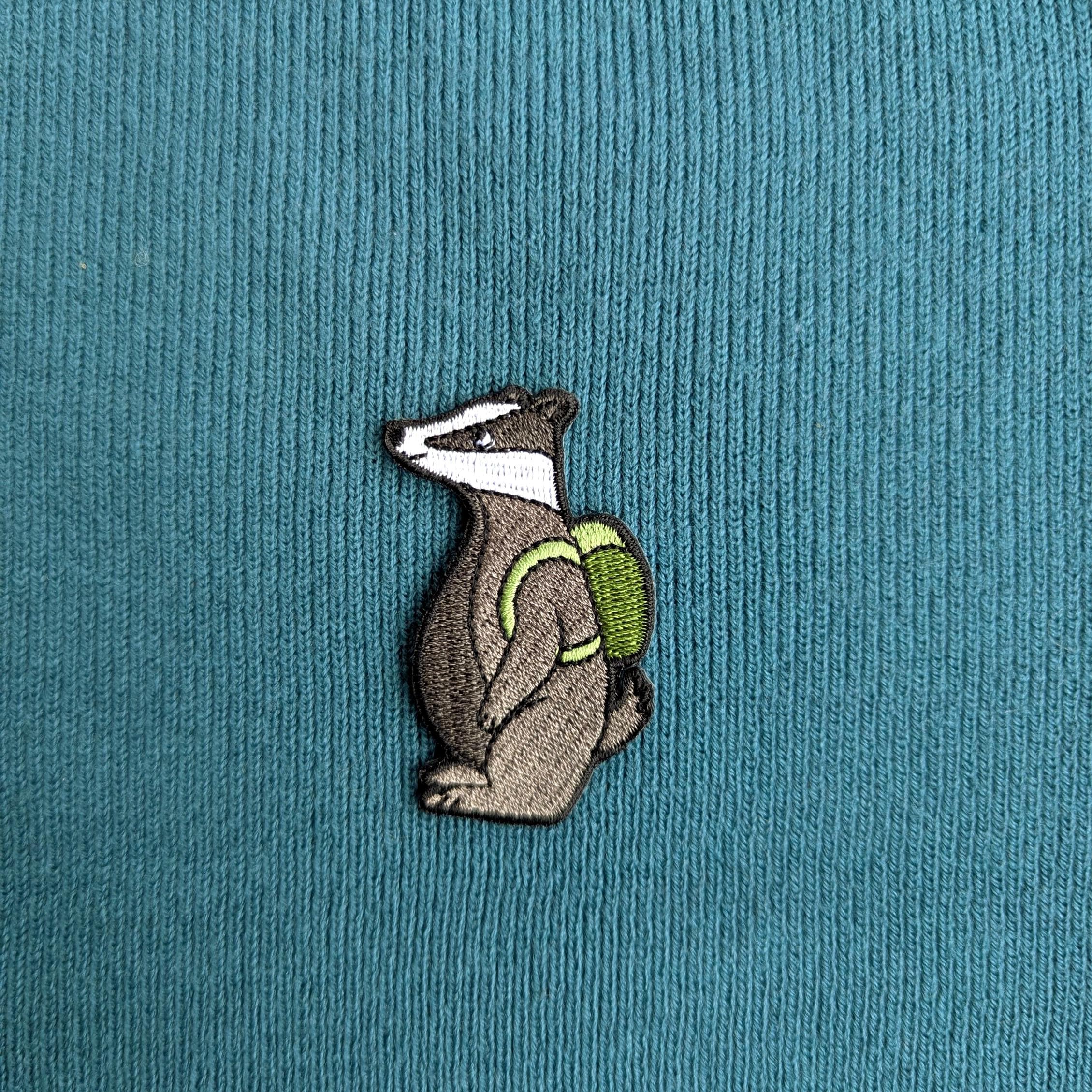 Embroidered badger with a green backpack on a teal fabric background