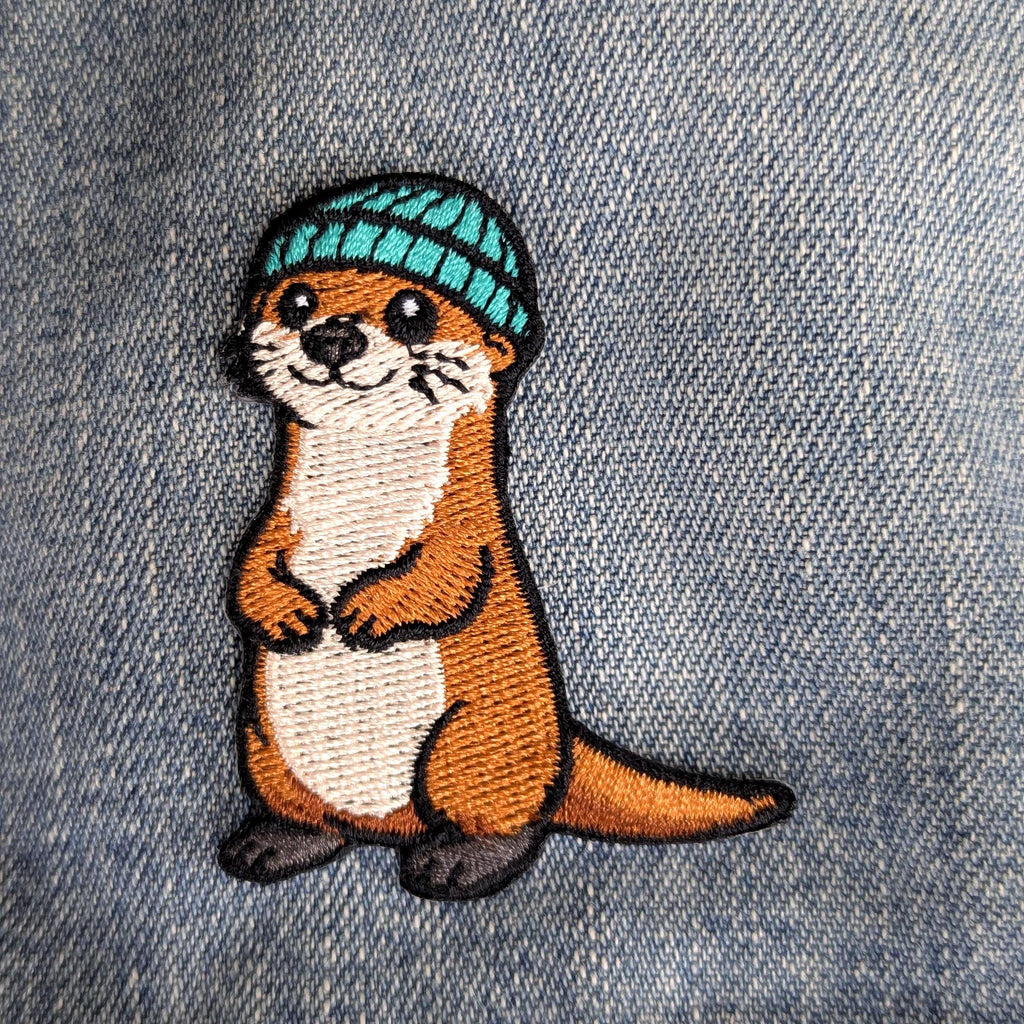 Embroidered otter patch with a blue hat on denim fabric