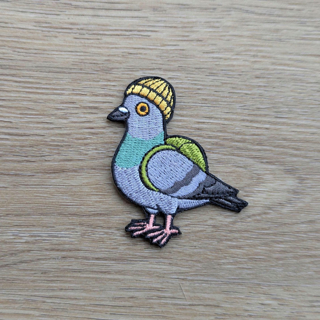 Embroidered patch of a pigeon wearing a yellow hat on a wooden surface