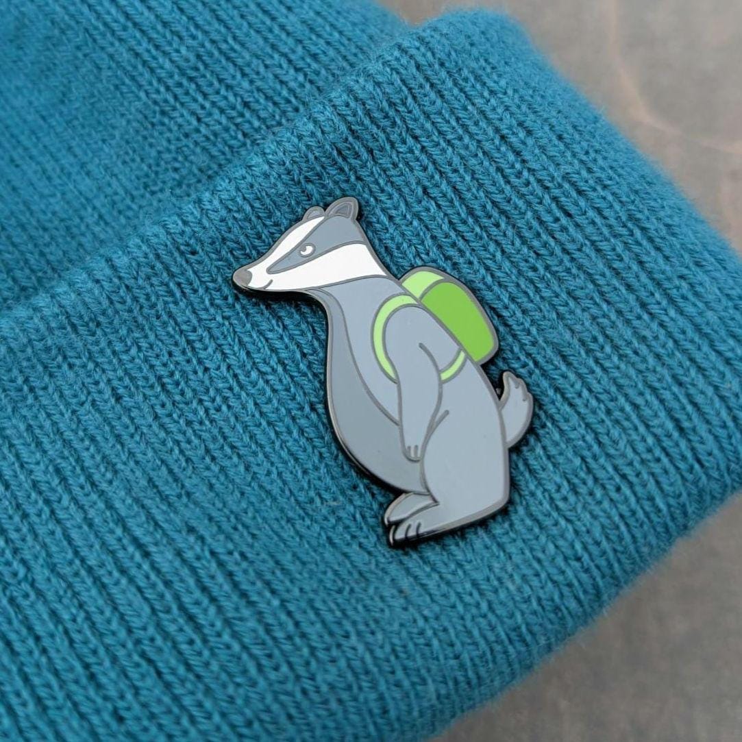 Badger pin with a green backpack on a blue fabric background
