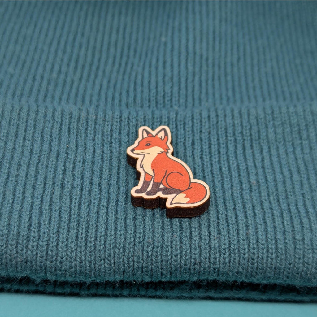 Wooden fox pin badge on a blue textured fabric background
