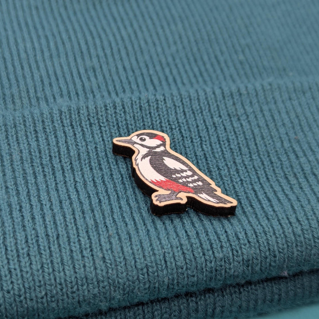 Woodpecker-shaped wooden pin on a textured teal fabric background