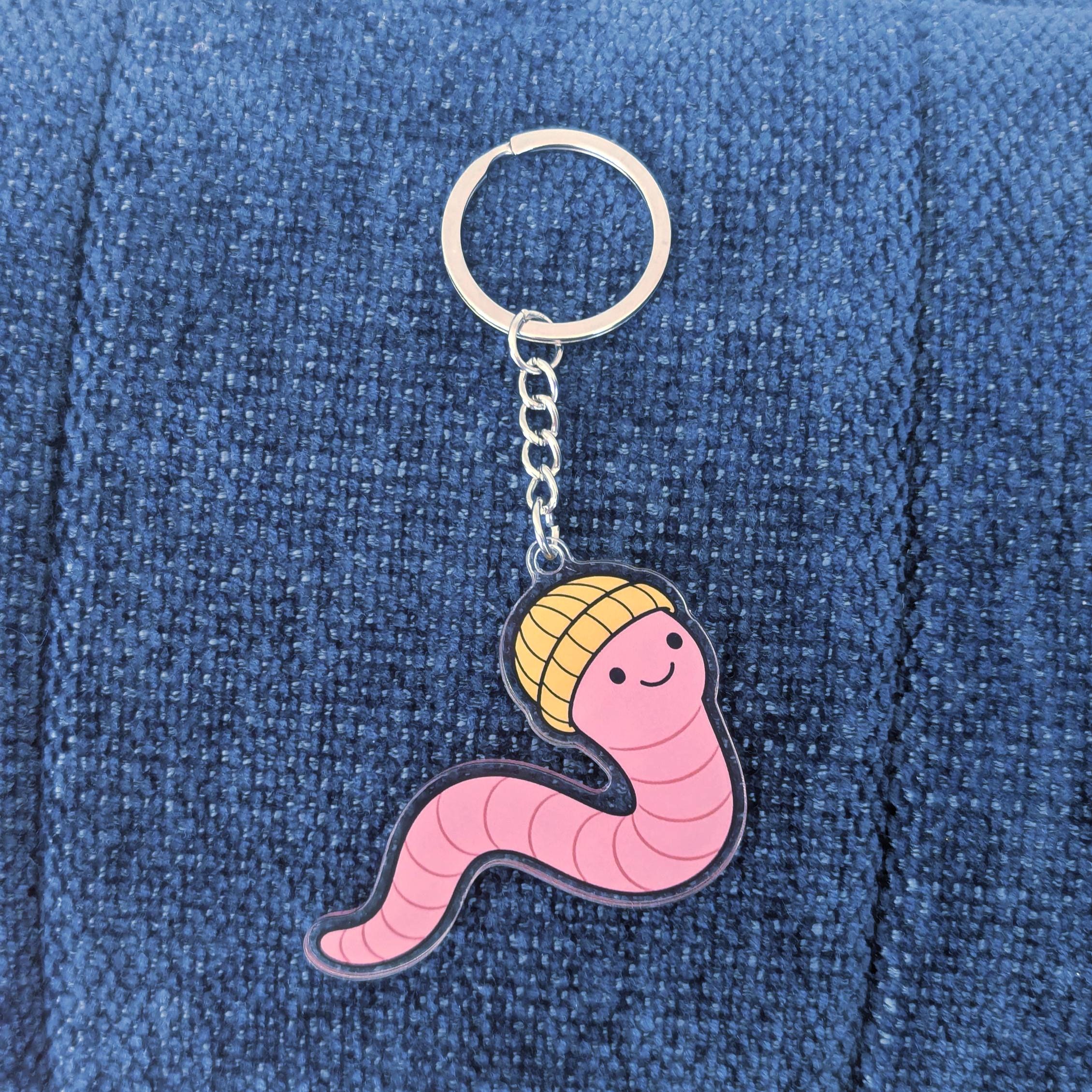 Keychain with a pink worm design wearing a yellow beanie on a blue denim background
