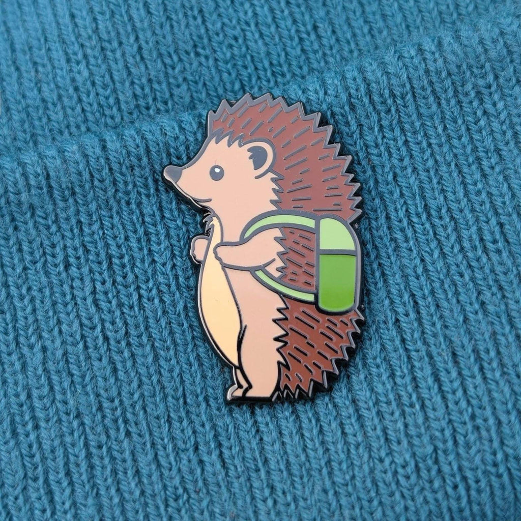 Hedgehog pin badge with a green backpack on a textured blue background