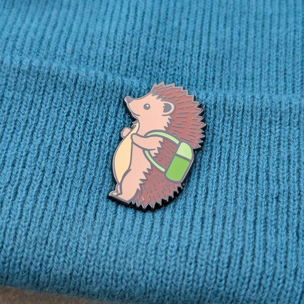 Hedgehog pin badge with a backpack pin on a blue knitted fabric background