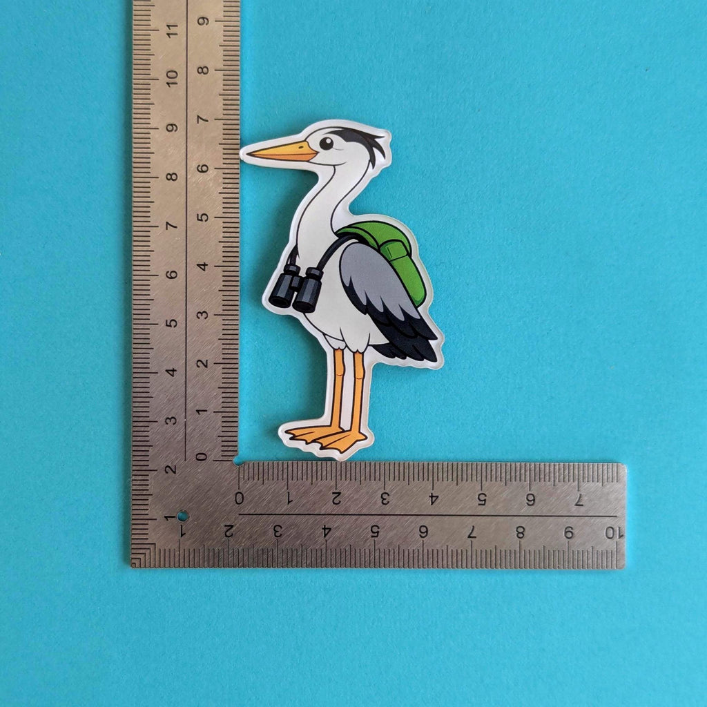 Fridge magnet of a heron with a backpack next to a ruler on a blue background