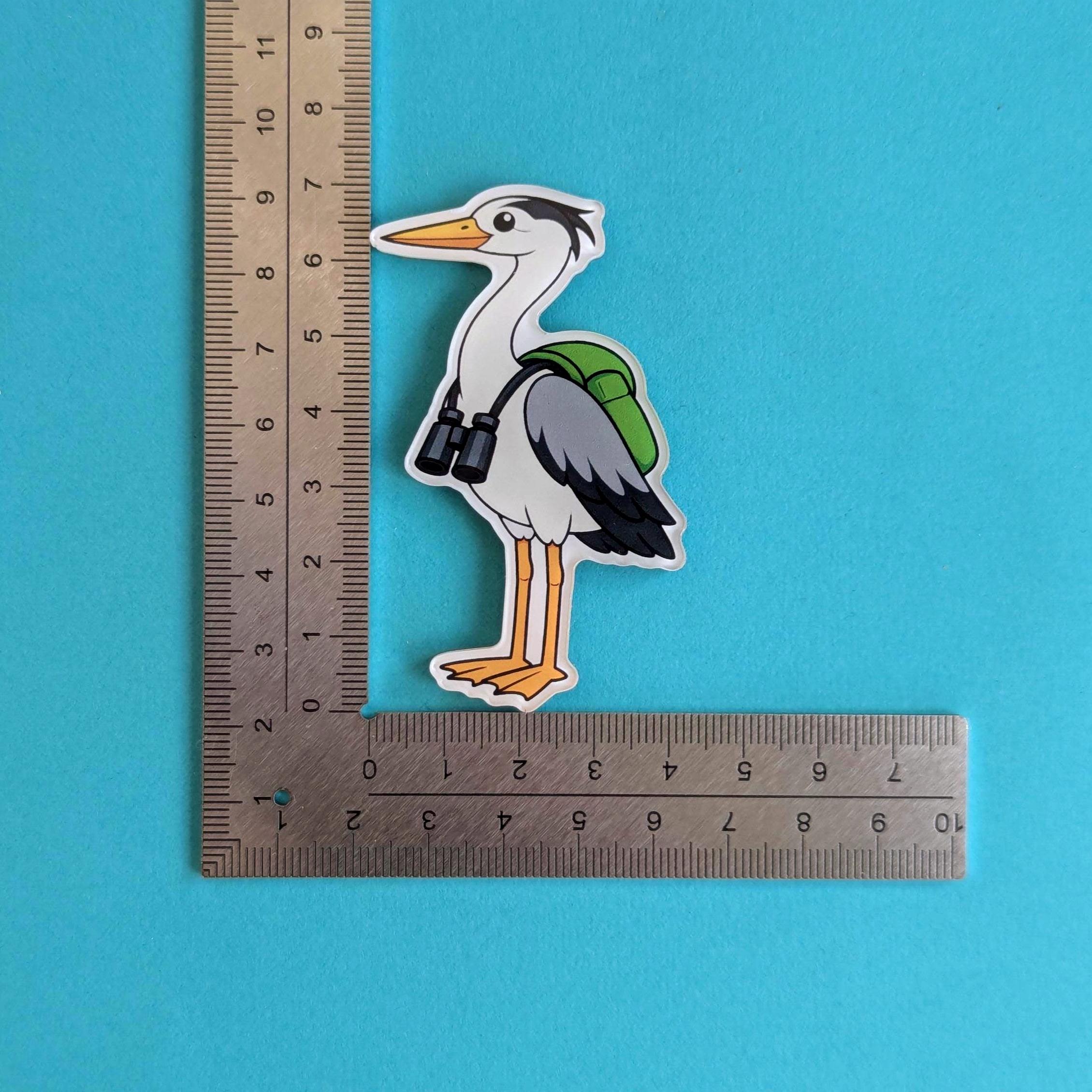 Fridge magnet of a heron with a backpack next to a ruler on a blue background