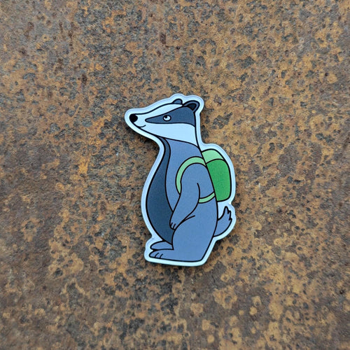 Fridge magnet of a badger with a green backpack on a textured brown surface