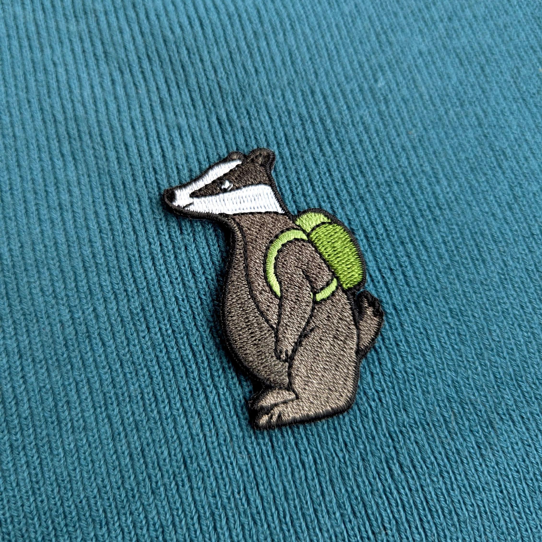 Embroidered badger patch with a green backpack on a teal fabric background