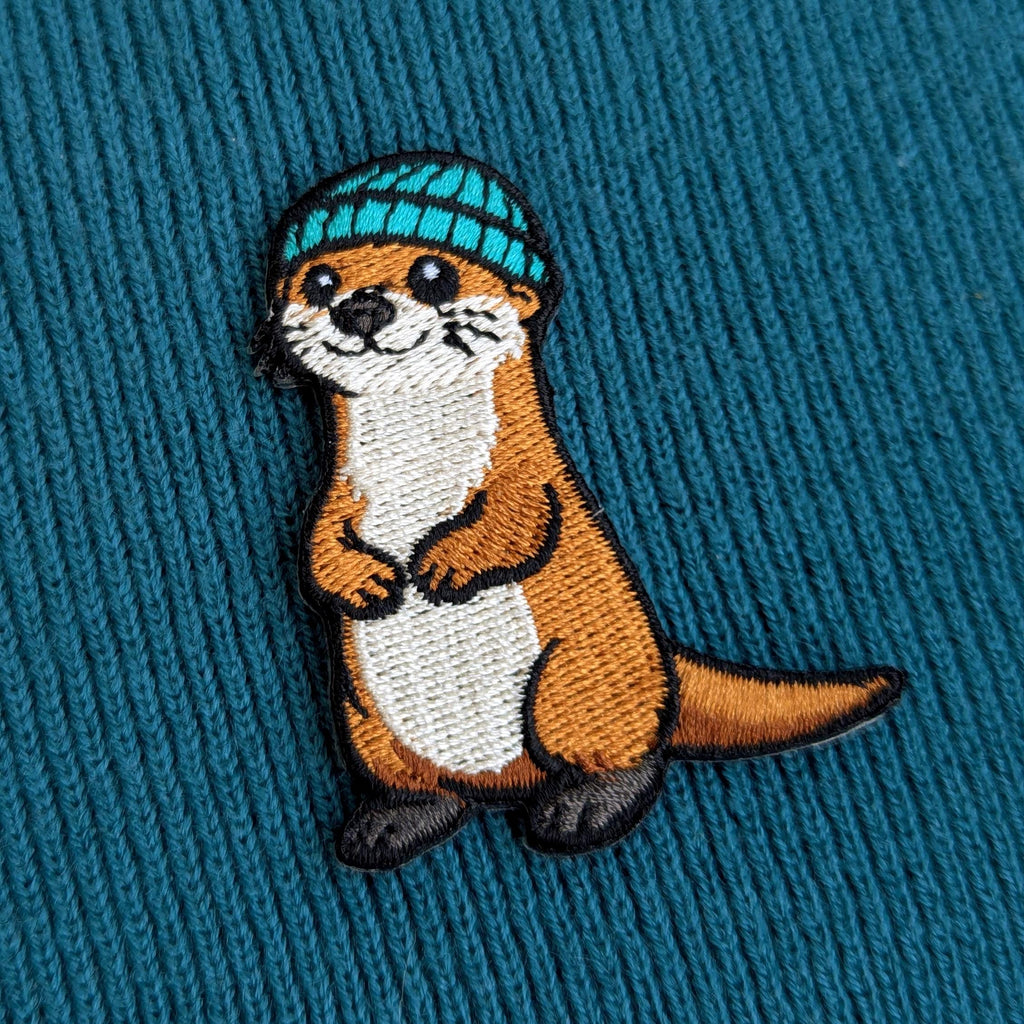 Embroidered otter patch with a blue hat on a textured blue background