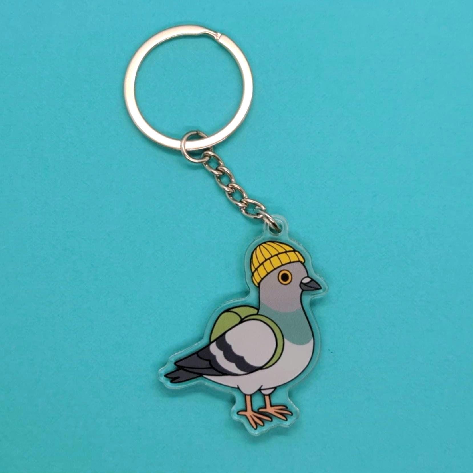 Keychain with a pigeon design wearing a yellow hat on a blue background