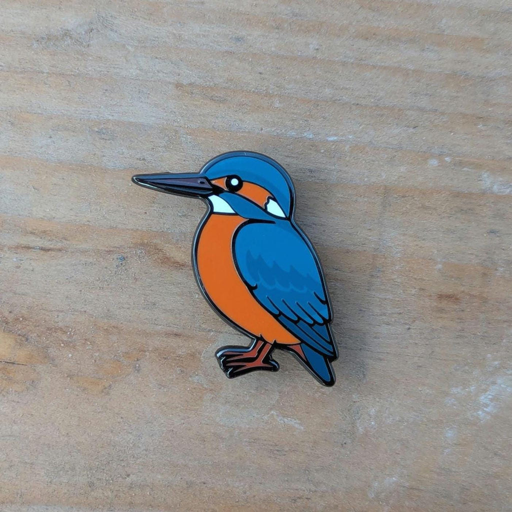Enamel pin of a blue and orange kingfisher on a wooden surface