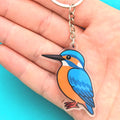 Keychain with a blue and orange bird design held in a hand against a turquoise background
