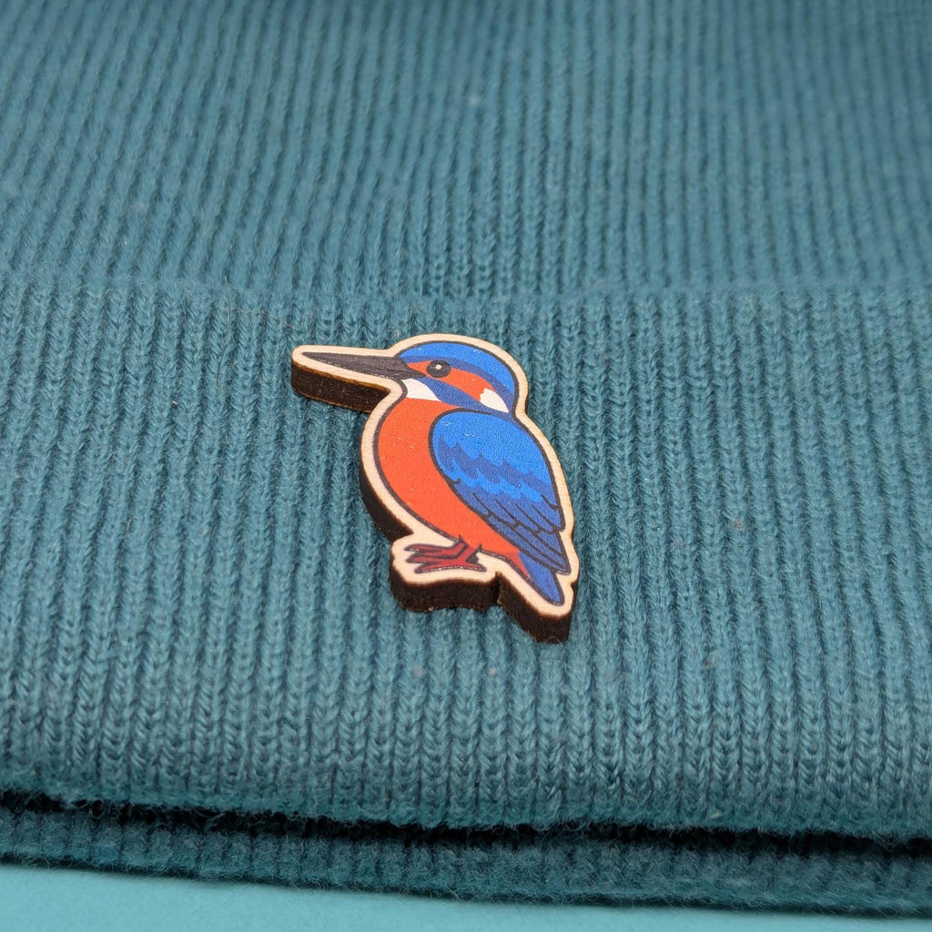 Wooden kingfisher bird pin on a teal knitted fabric background