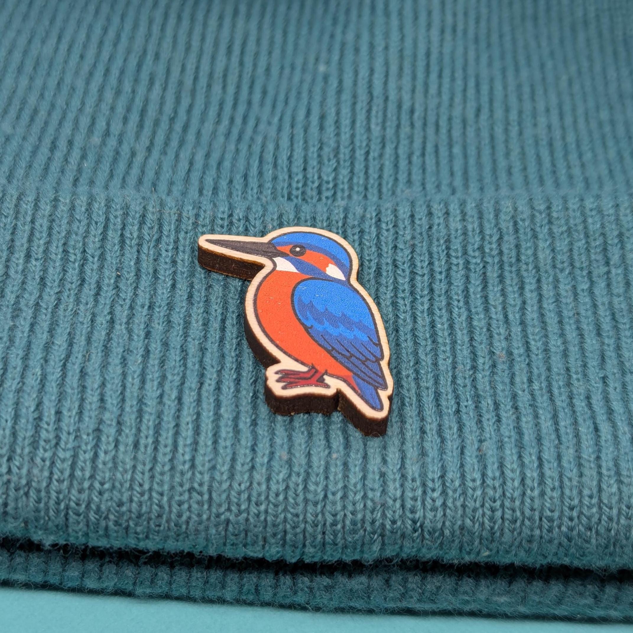 Wooden kingfisher bird pin on a teal knitted fabric background