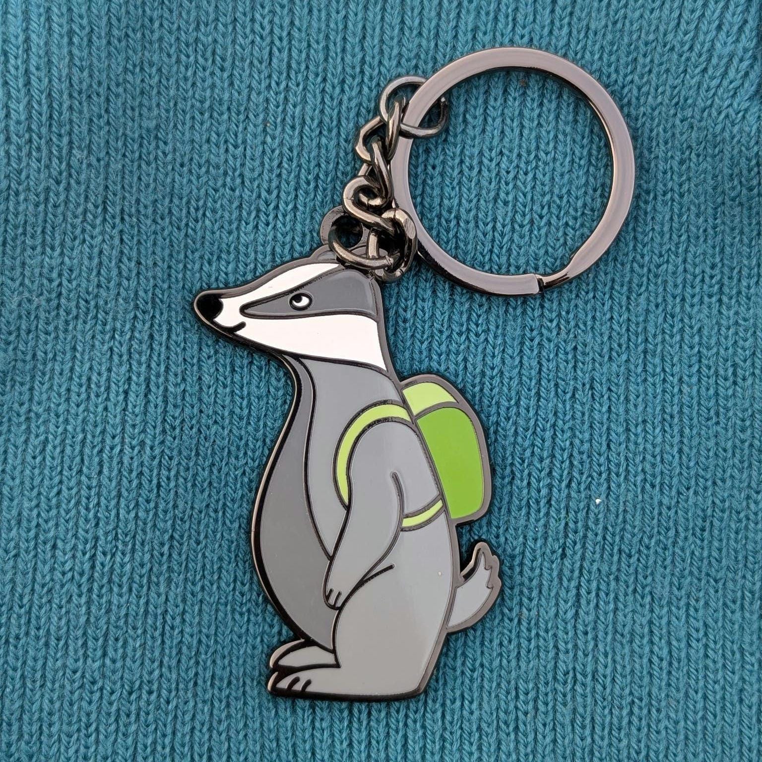 Keychain with a badger design wearing a green backpack on a blue textured background