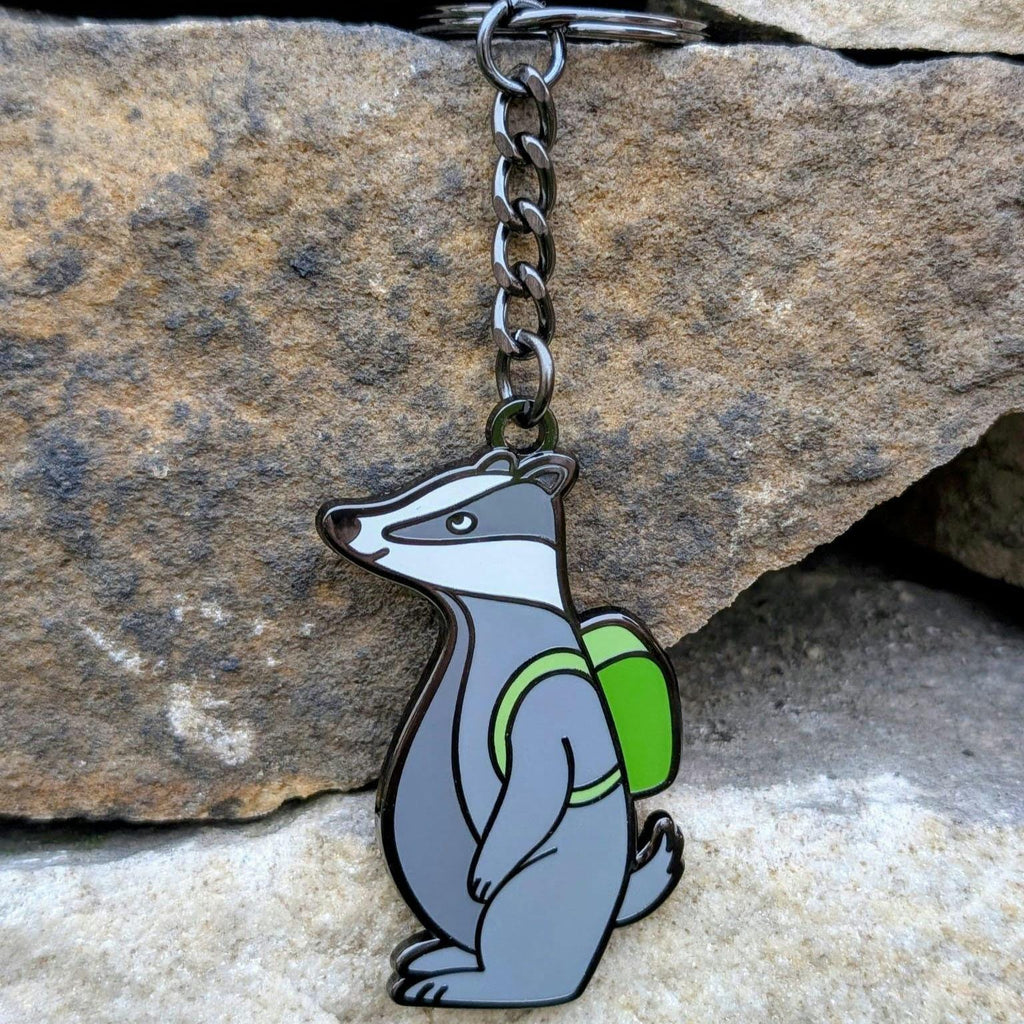 Keychain with a badger design wearing a green backpack against a stone background